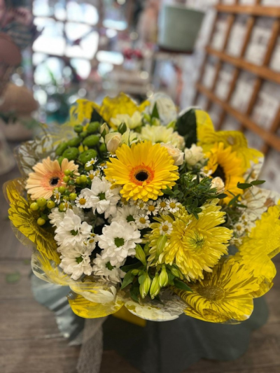 Golden Sunshine - A beautifully handcrafted hand-tied bouquet presented in water, featuring a fresh blend of seasonal blooms in bright yellow, white and soft cream tones.